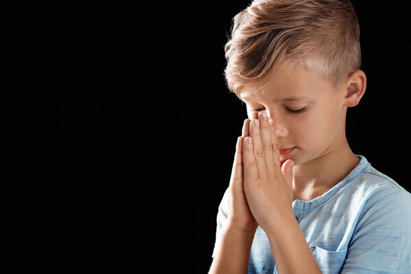 Little boy with hands clasped together for prayer on black background. Space for text