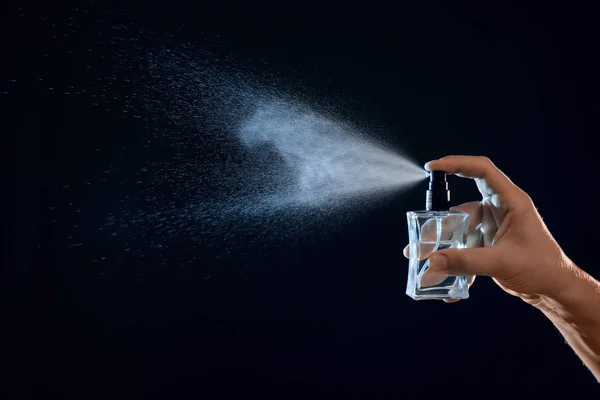 Young man spraying perfume on black background, closeup