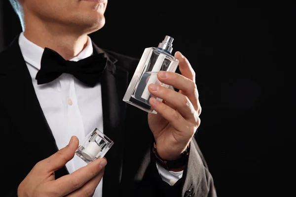 Young man with perfume bottle on black background, closeup