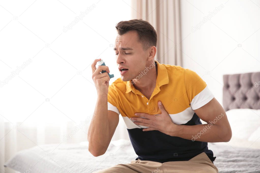 Young man with asthma inhaler on bed in light room