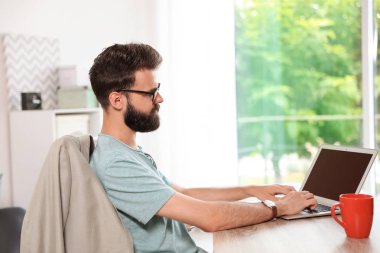 Evde dizüstü bilgisayarla çalışan sakallı genç bir adam.