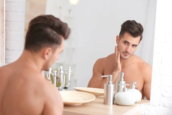Young man with stubble ready for shaving near mirror in bathroom