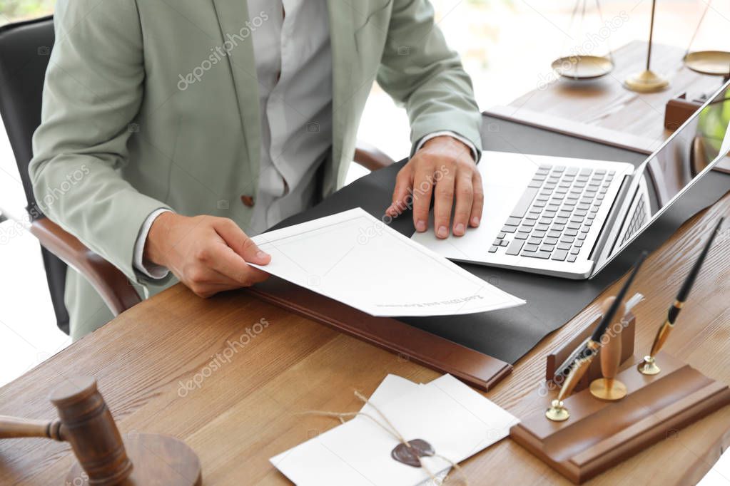 Male notary with documents and laptop at table in office, closeup