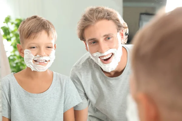 Father and son with shaving foam on faces in bathroom