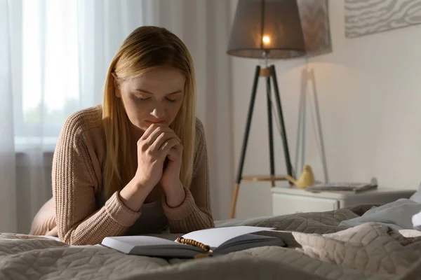 Religious young woman praying over Bible in bedroom