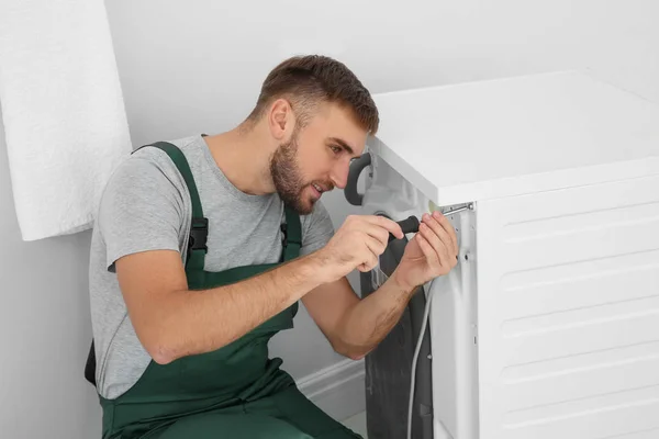 Young plumber fixing washing machine in bathroom