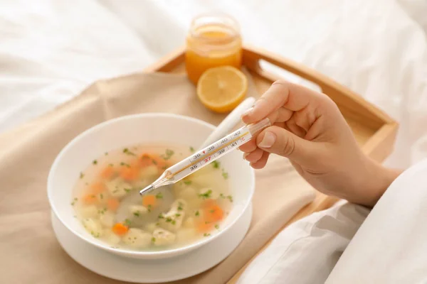 ベッド クローズ アップの皿のインフルエンザを治すため温度計と新鮮な自家製スープの病気の女性 — ストック写真