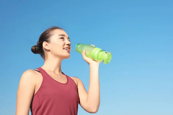 在阳光明媚的日子里 年轻的运动女子在蓝天的映衬下喝瓶子里的水 文本的空间 — 图库照片