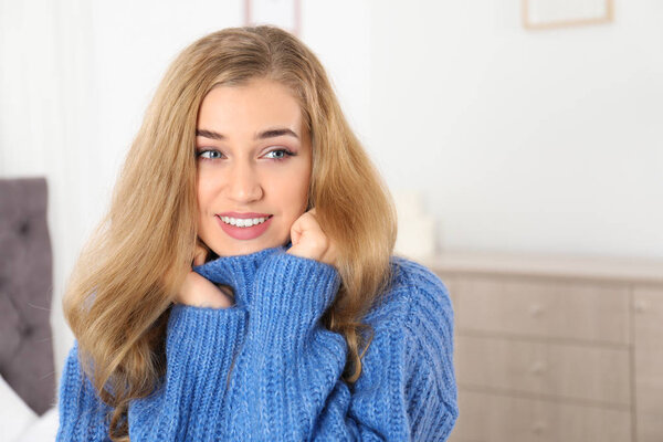 Beautiful smiling young woman in cozy warm sweater at home. Space for text