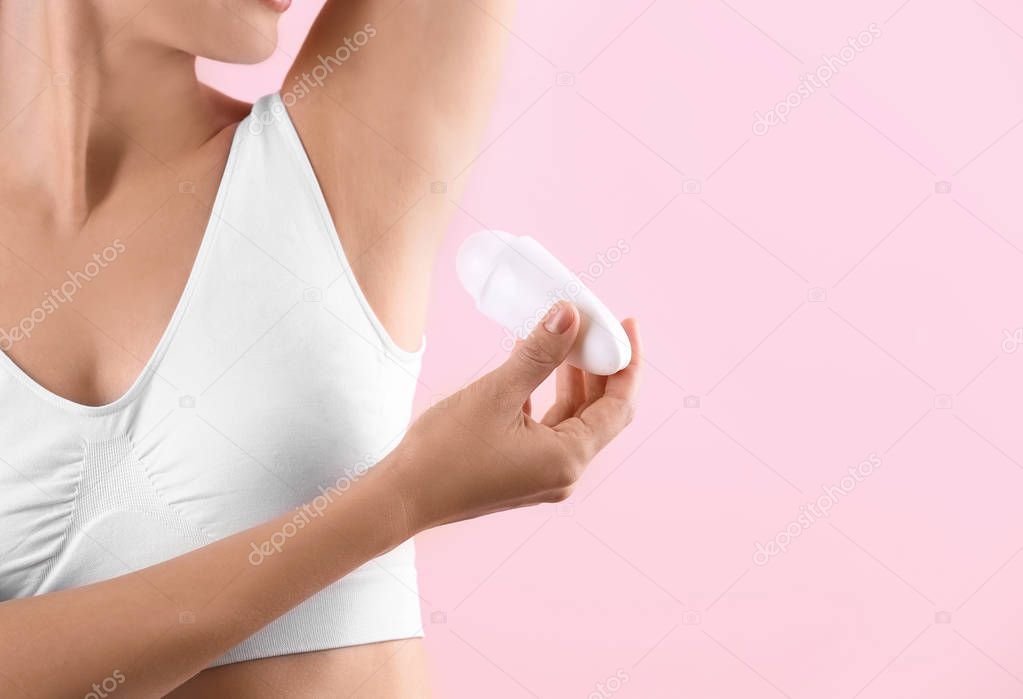 Young woman using deodorant on color background, closeup. Space for text