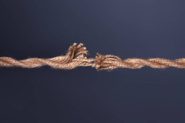 Растянутая изношенная верёвка рвётся на тёмном фоне
