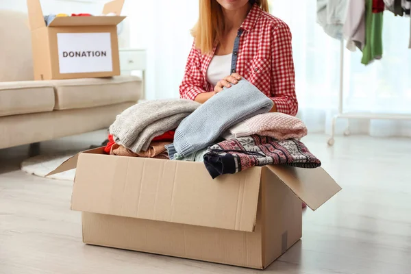 Woman packing clothes into donation box in living room