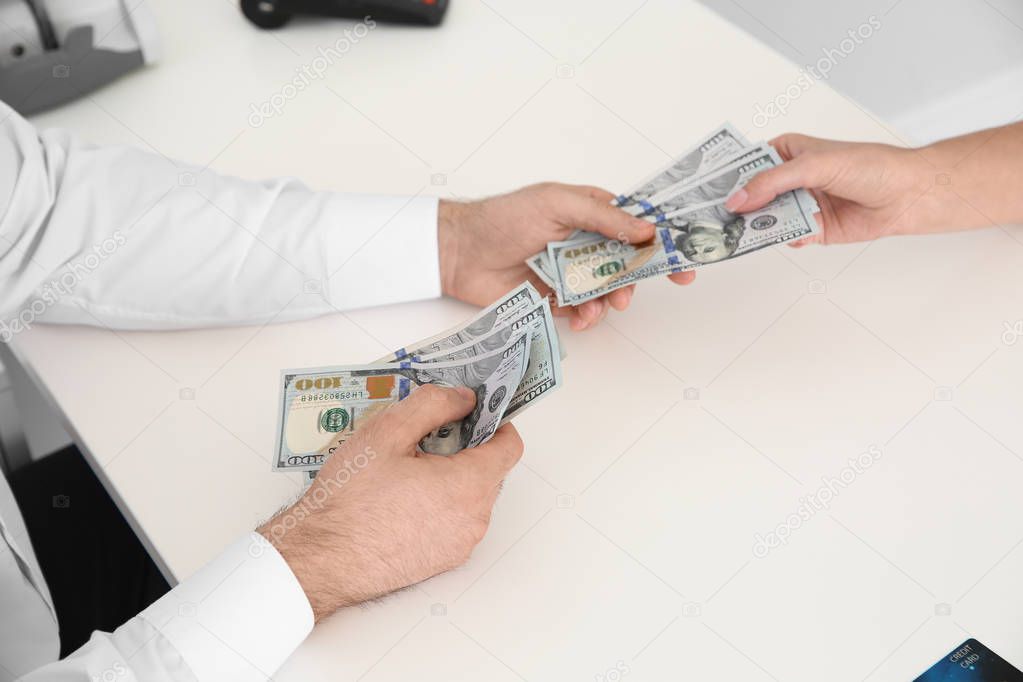 Male teller giving money to woman at table, closeup