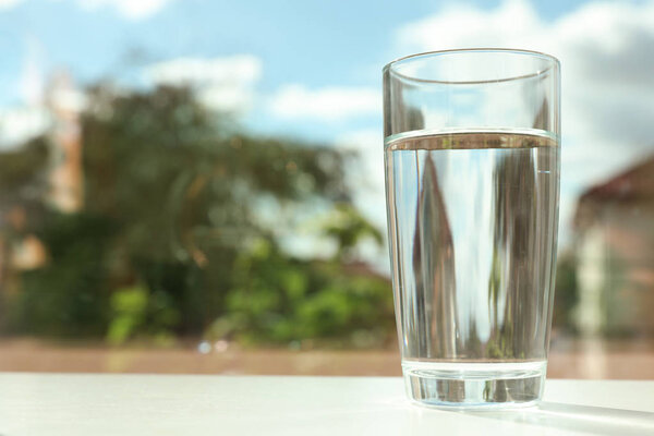Glass of fresh water on table outdoors. Space for text