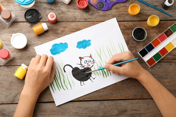 Girl painting picture of cat on table, top view