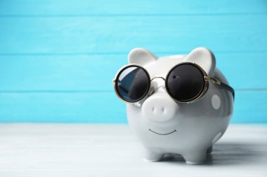 Piggy bank with sunglasses on table. Space for text clipart