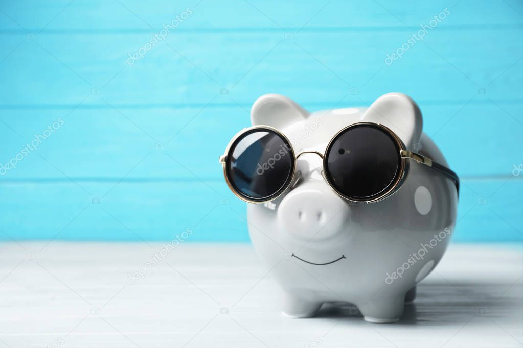 Piggy bank with sunglasses on table. Space for text