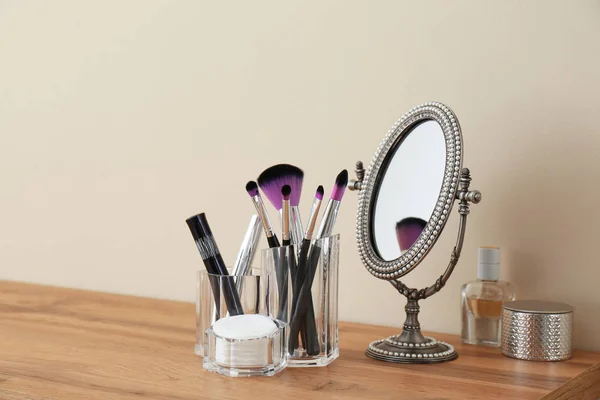 Organizer with cosmetic products for makeup and mirror on table against light wall