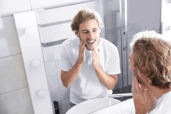 浴室の鏡の近く石鹸で顔を洗う若い男 — ストック写真