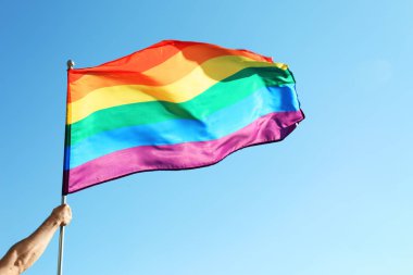 Gökkuşağı Lgbt bayrağı mavi gökyüzü arka plan üzerinde tutan eşcinsel adam. Metin için yer