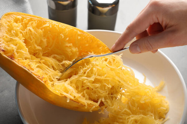 Woman scraping flesh of cooked spaghetti squash with fork at table, closeup