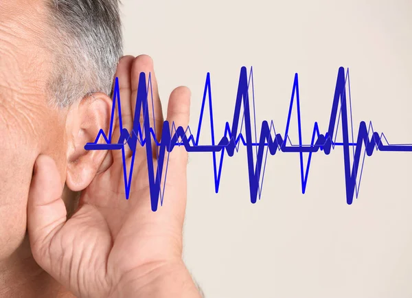 Mature man with symptom of hearing loss on color background. Medical test