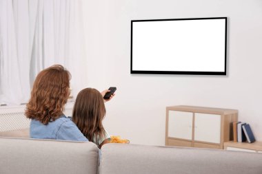 Anne ve kızı kanepede oturan ve evde, alan tasarım ekranında Tv izlerken uzaktan kumanda ile. Eğlence ve eğlence