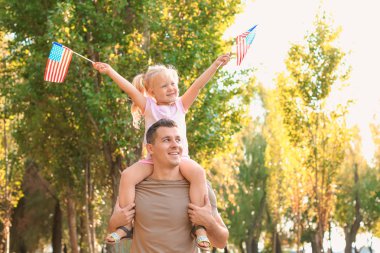 Adam kızı Amerikan bayrakları ile parkta güneşli günde tutarak.