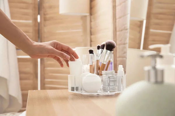 Woman taking tube with cream from organizer for cosmetic products on table