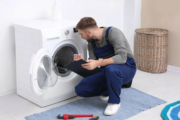 Young plumber with clipboard near washing machine in bathroom
