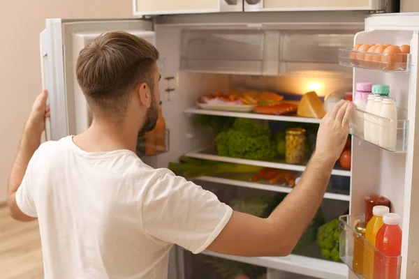 若い男を自宅の冷蔵庫で食品を選択します — ストック写真