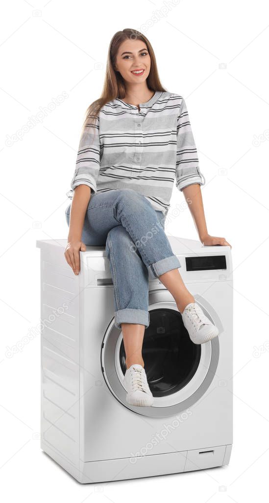 Young woman sitting on washing machine against white background. Laundry equipment