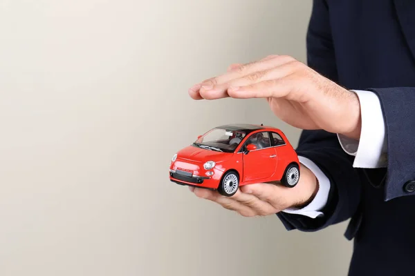 Male Insurance Agent Holding Toy Car Light Background Closeup Space — Stock Photo, Image