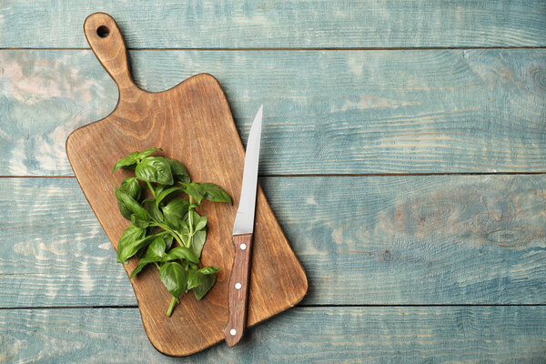Board with fresh basil and knife on wooden background, top view. Space for text