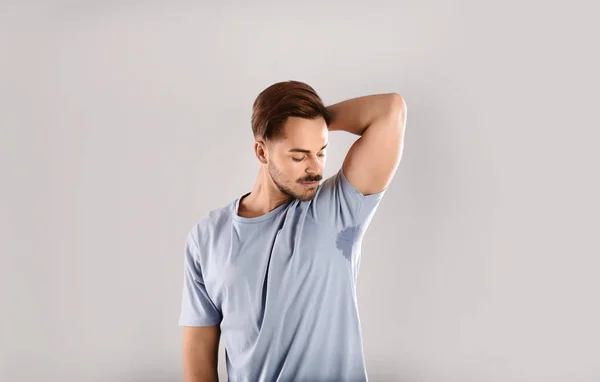 Sweaty man with stain on t-shirt against gray background. Using deodorant