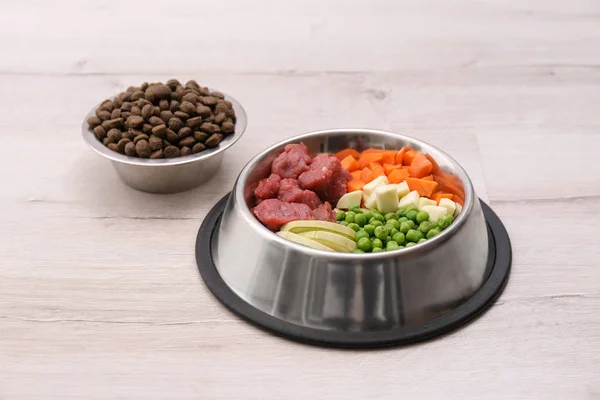 Bowls with dry and natural dog food on light background