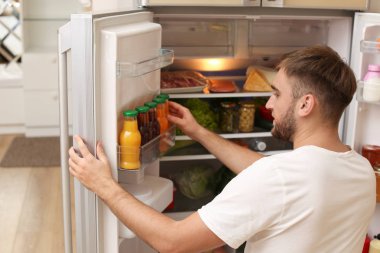 Genç adam alarak şişe suyu mutfakta buzdolabı