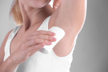 Deodorant gri arka plan üzerinde closeup kullanan genç kadın
