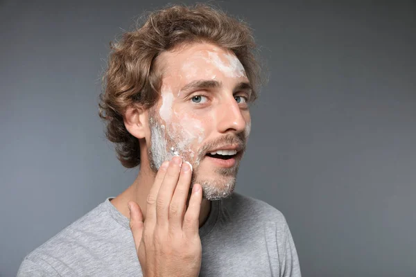 Young man washing face with soap on grey background