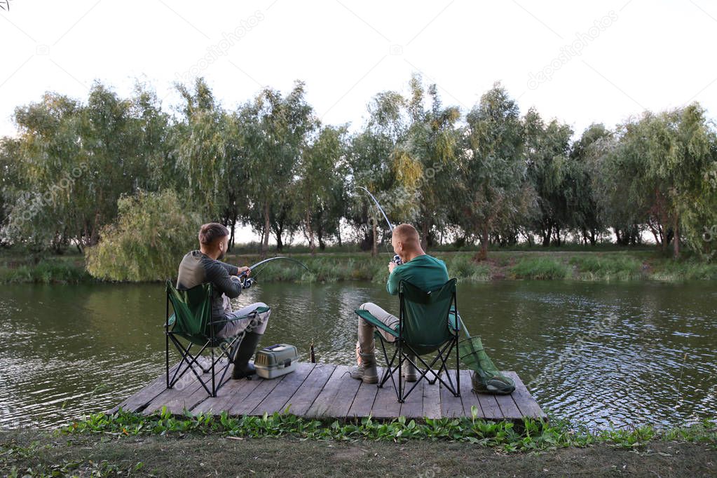 Friends fishing on wooden pier at riverside. Recreational activity