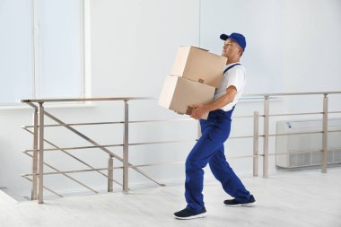 Man in uniform carrying carton boxes indoors. Posture concept clipart