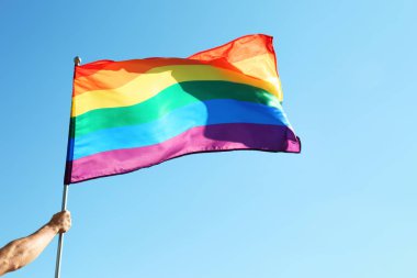 Gökkuşağı Lgbt bayrağı mavi gökyüzü arka plan üzerinde tutan eşcinsel adam
