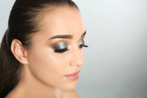 Portrait of young woman with eyelash extensions and makeup on light background. Space for text