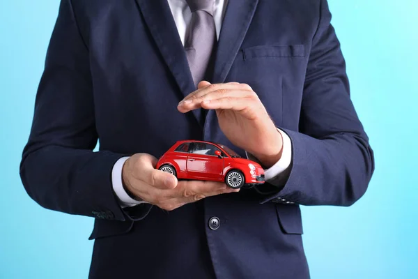 Männlicher Versicherungsvertreter Hält Spielzeugauto Auf Farbigem Hintergrund Nahaufnahme — Stockfoto
