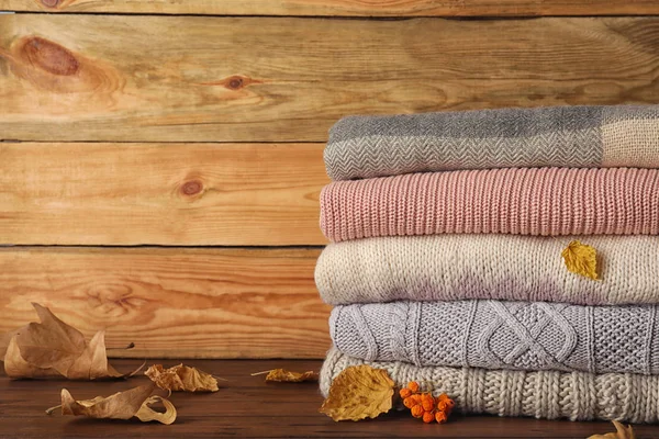 Tumpukan Pakaian Hangat Dengan Daun Musim Gugur Atas Meja Kayu — Stok Foto