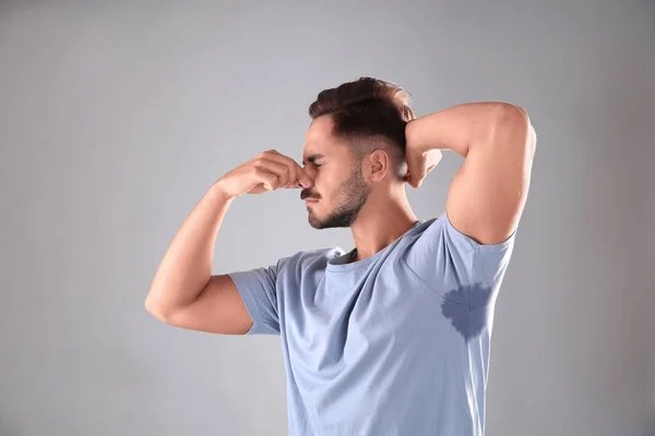 Sweaty man with stain on t-shirt against gray background. Using deodorant