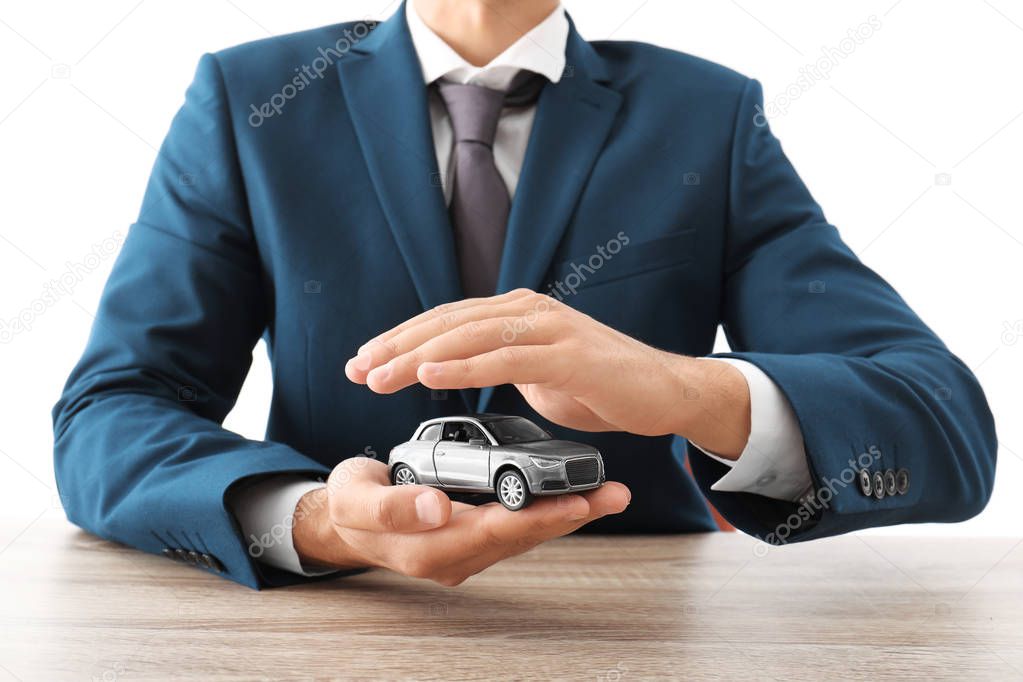 Insurance agent holding toy car in hands over table against white background