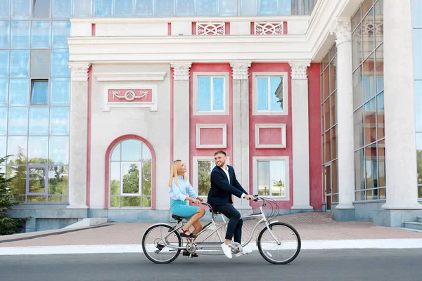 Couple riding tandem bike on city street