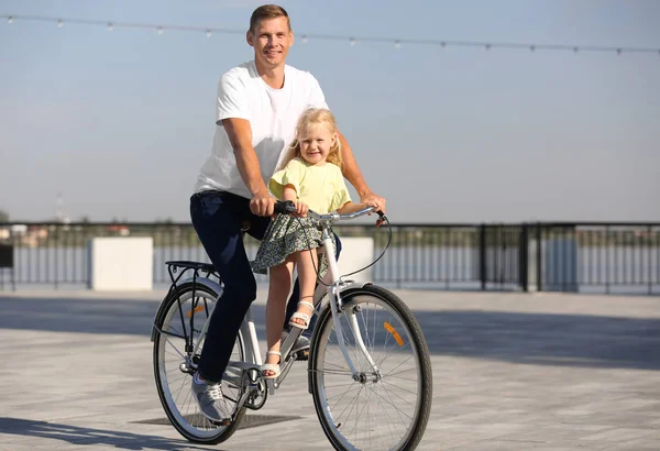 Father and daughter riding bicycle outdoors on sunny day