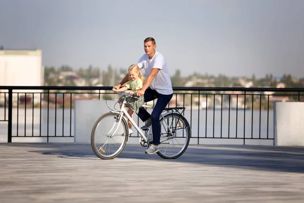 Father and daughter riding bicycle outdoors on sunny day